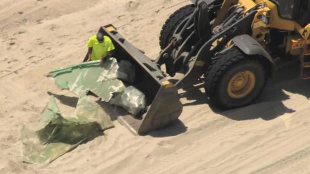 A worker cleans up pieces of wind turbine blade that washed ashore on Nantucket.